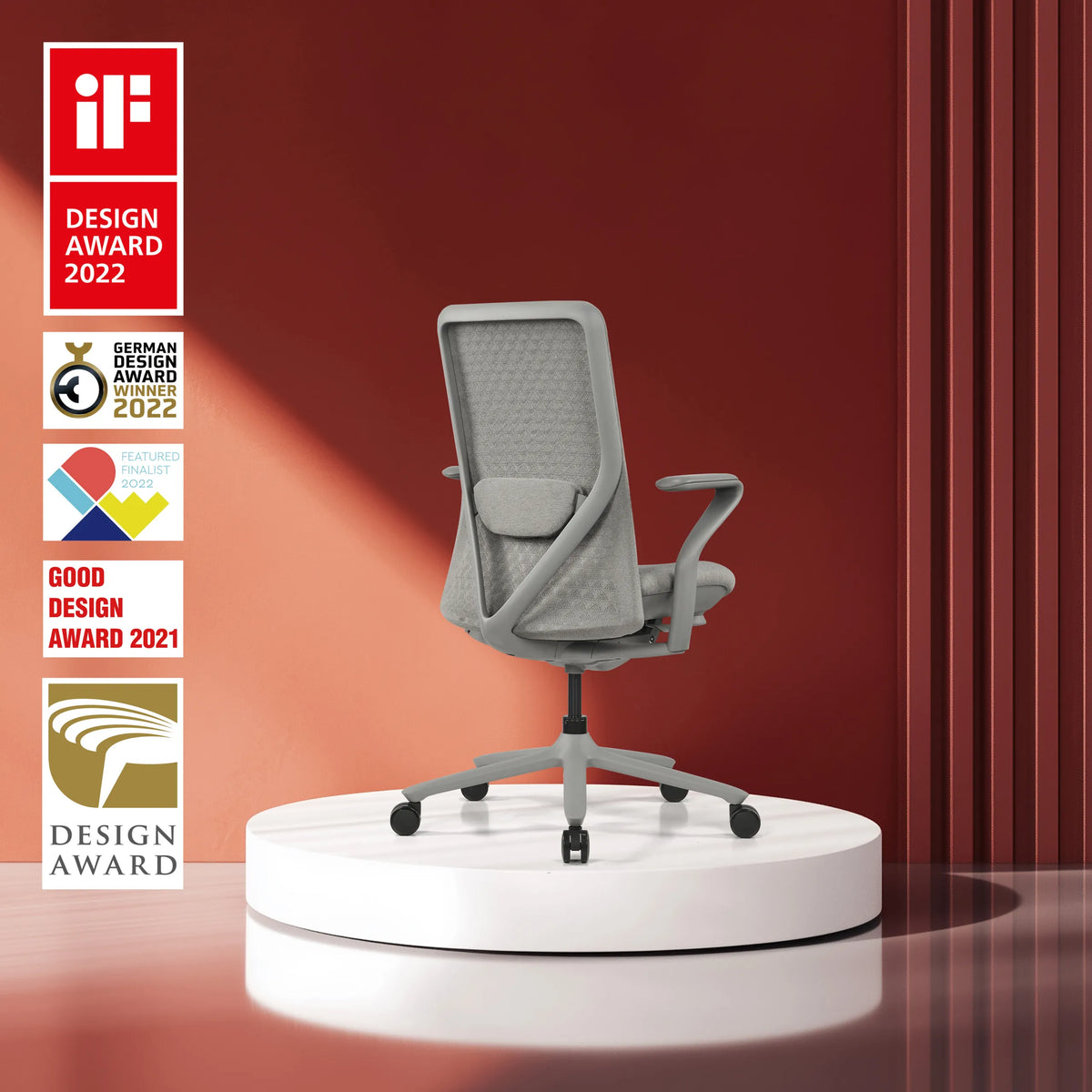Harmaa High End -toimistotuoli VERVIO verkkoselkänojalla valkoisella korokkeella punaista taustaa vasten, valmistaja hjh OFFICE