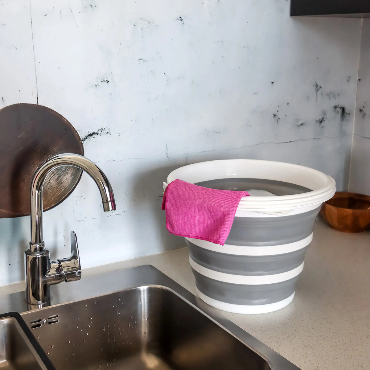 Harmaanvalkoinen Kokoontaitettava kontti CLEAN SILR ja vaaleanpunainen liina työtasolla pesualtaan vieressä, valmistaja hjh OFFICE