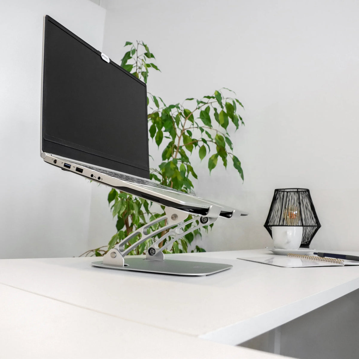 Hopeinen LAPTOP STAND -alusta säädettävällä jalustalla ja kannettava tietokone valkoisella pöydällä, valmistaja hjh OFFICE