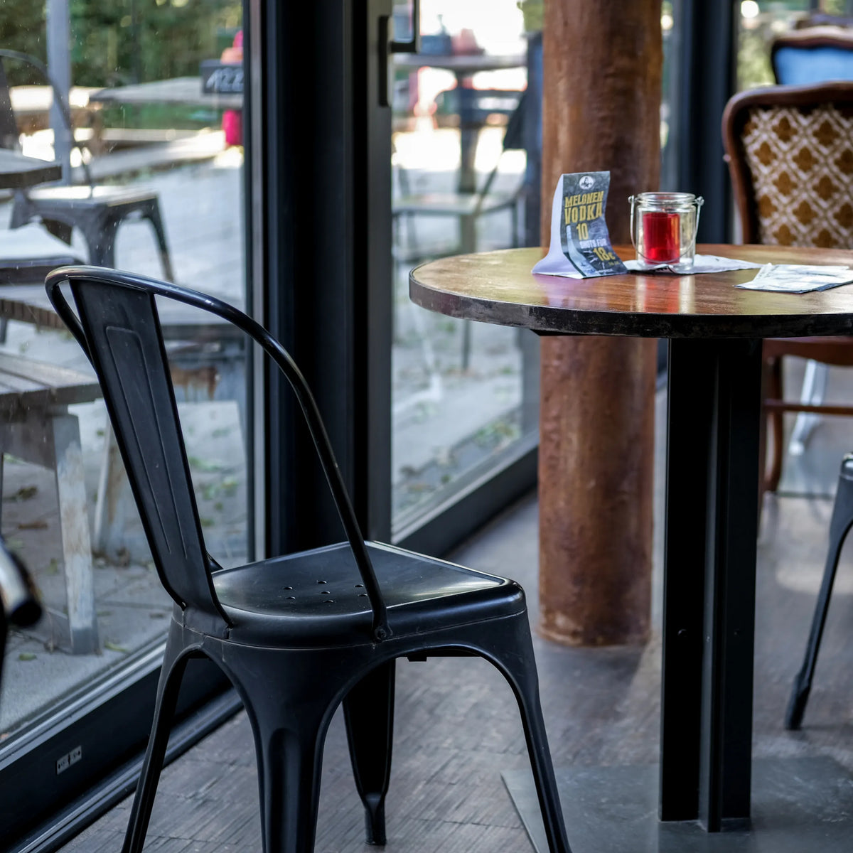 Musta Bistrotuoli VANTAGGIO BRUSH, jossa on kaareva selkänoja, pyöreän pöydän ääressä, valmistaja hjh OFFICE