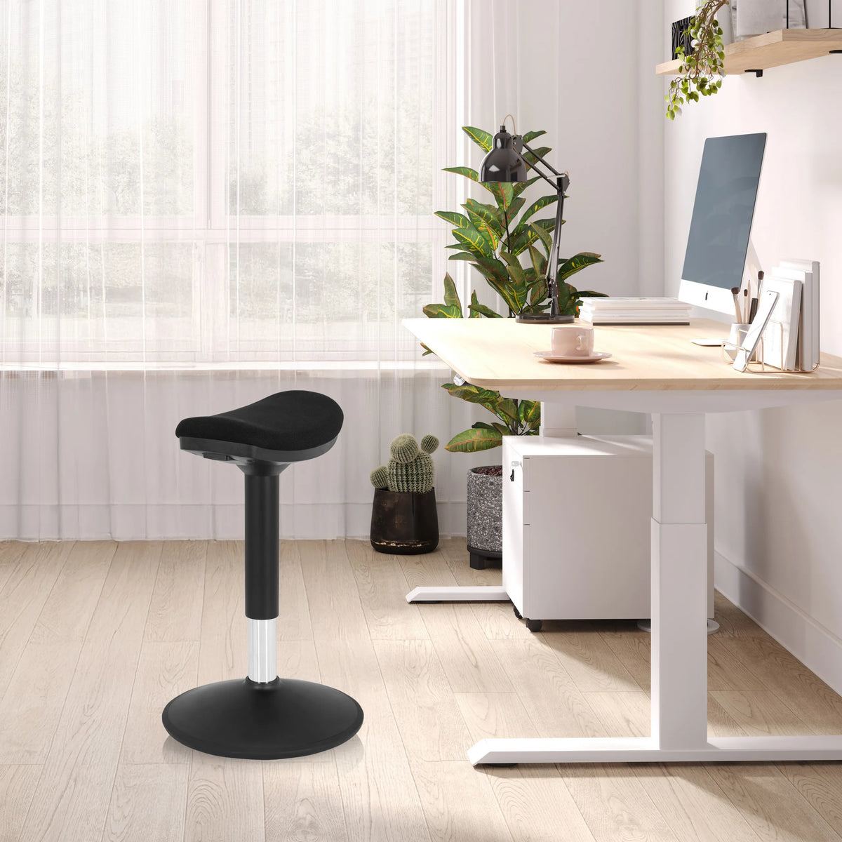 Schwarze Stehhilfe BALANCE SIT I B mit rundem Standfuß und gepolsterter Sitzfläche in einem hellen Büro von hjh OFFICE